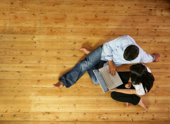 couple assis sur parquet avec ordinateur portable